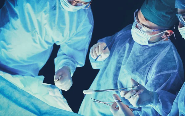 Chirurgen aan het werk in de operatiekamer, blauw getint. Medisch team voert operatie uit — Stockfoto