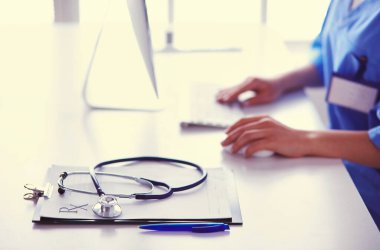 Kadın doktor masada oturuyor ve hastanede dizüstü bilgisayarla çalışıyor.