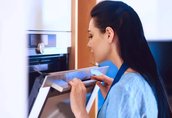 Hermosa joven comprobando cómo le va a su pastel en el horno — Foto de Stock