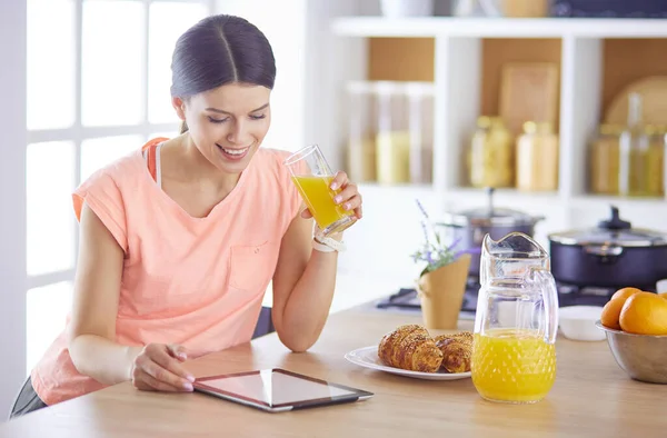 Vacker ung kvinna med hjälp av en digital tablett i köket — Stockfoto