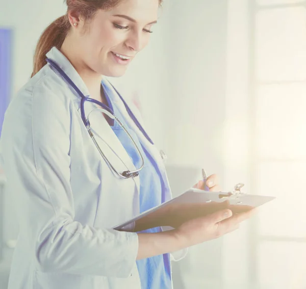 Arzt mit Stethoskop, ein Notizbuch in der Hand. Nahaufnahme einer Ärztin beim Ausfüllen medizinischer Formulare am Klemmbrett, während sie gerade im Krankenhaus steht — Stockfoto