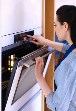 Güzel genç bayan pastasının fırında ne yaptığını kontrol ediyor.