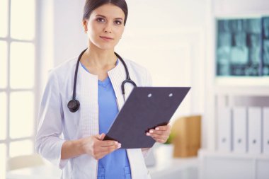 Doktor muayenehanesinde steteskopla gülümseyen genç bir bayan doktor.