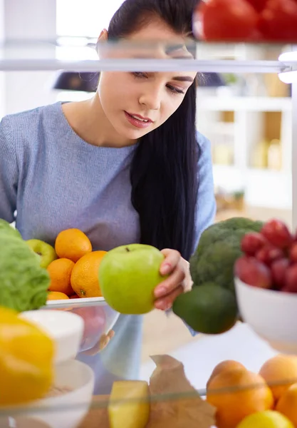 Smiling woman taking a fresh fruit out of the fridge, healthy food concept — Stock Photo, Image