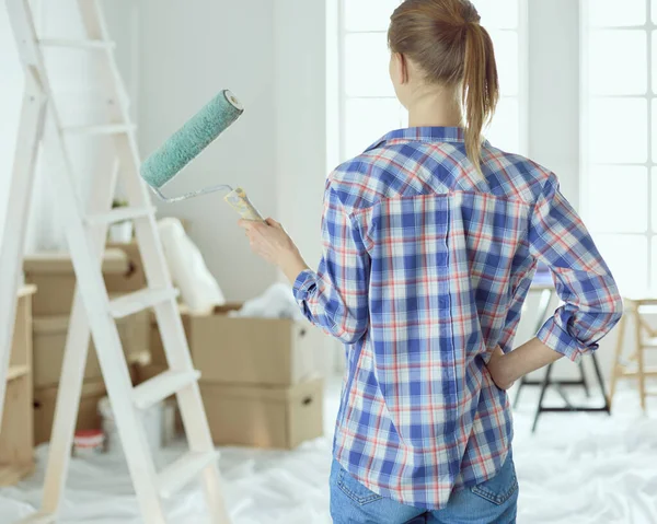Красивая кудрявая женщина рисует внутреннюю стену дома с помощью краски ролика — стоковое фото