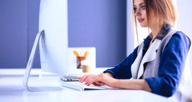 Ofis masasında çalışan ve dizüstü bilgisayarla yazan kendine güvenen genç bir iş kadını.