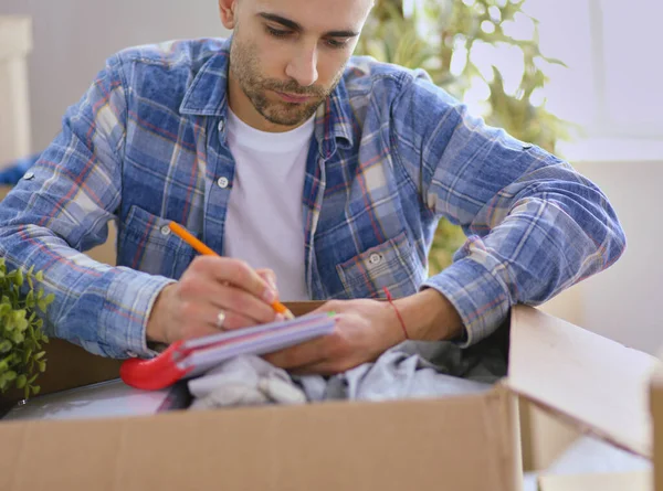 A moving man sitting on the floor in empty apartment, Among the Boxes, Checking the List of Things