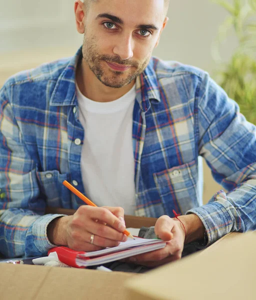 Un uomo in movimento seduto sul pavimento in appartamento vuoto, Tra le scatole, Controllare la lista delle cose — Foto Stock