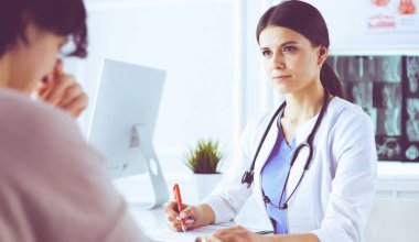 Kadın doktor hastane danışma odasında bir hastayı sakinleştiriyor, elini tutuyor.