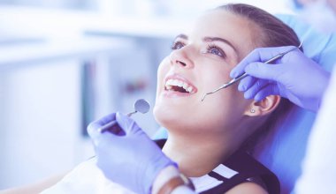 Dişçi muayenehanesinde diş muayenesi yapan ağzı açık genç bir kadın hasta..