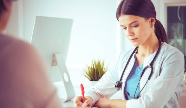 Doktor ve hasta hastane danışma odasında tıbbi sorunları tartışıyorlar. Doktor hasta formunu dolduruyor.