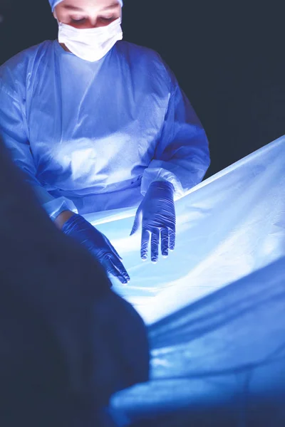 Equipo de médicos en cirugía en un fondo oscuro. — Foto de Stock