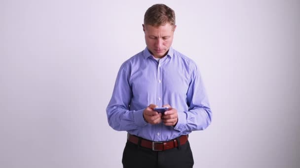 A young businessman stands by the wall and looks at the screen of his smartphone. — Stock Video
