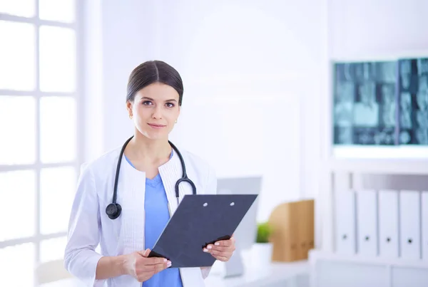 Mladá usměvavá doktorka se stetoskopem drží složku v ordinaci lékaře — Stock fotografie