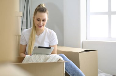 Güzel bekar bir kadın kutuları açıyor ve yeni bir eve taşınıyor. Bir kadın buraya bak tablet