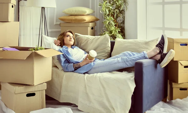 Szczęśliwa młoda kobieta leżąca na kanapie w nowym domu, pijąca kawę lub herbatę — Zdjęcie stockowe