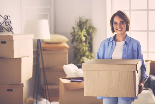 Egy csinos nő portréja, amint dobozt tart az új otthonában. — Stock Fotó