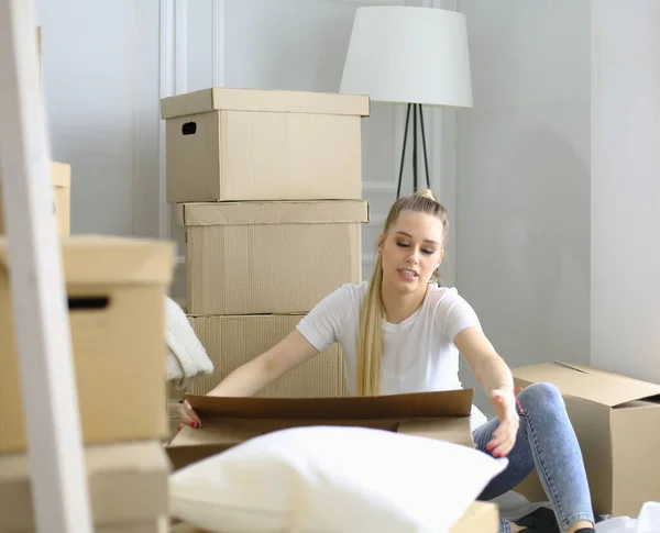 Красивая одинокая девушка распаковывает коробки и переезжает в новый дом. Женщины смотрят сюда планшет — стоковое фото