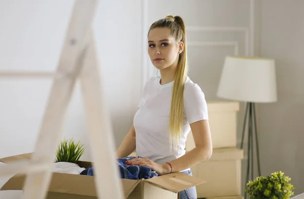 Una hermosa mujer joven soltera desempacando cajas y mudarse a un nuevo hogar. Una mujer mira aquí tableta —  Fotos de Stock