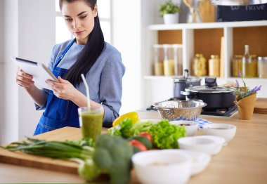 Mutfakta yemek yapmak için tablet bilgisayar kullanan genç bir kadın.