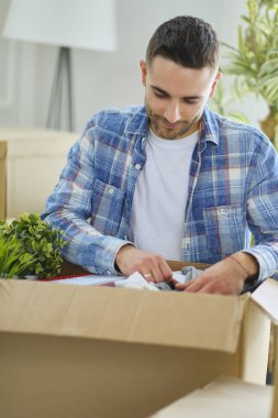 Taşınan bir adam boş bir dairede oturuyor, Kutuların arasında, eşyaların listesini kontrol ediyor.