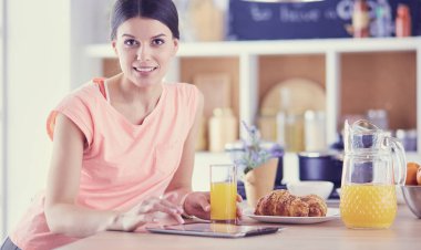 Mutfakta dijital tablet kullanan güzel genç bir kadın.