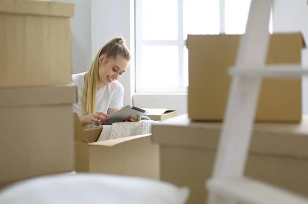 Uma bela mulher solteira desempacotar caixas e se mudar para uma nova casa. Uma mulher olha para aqui tablet — Fotografia de Stock