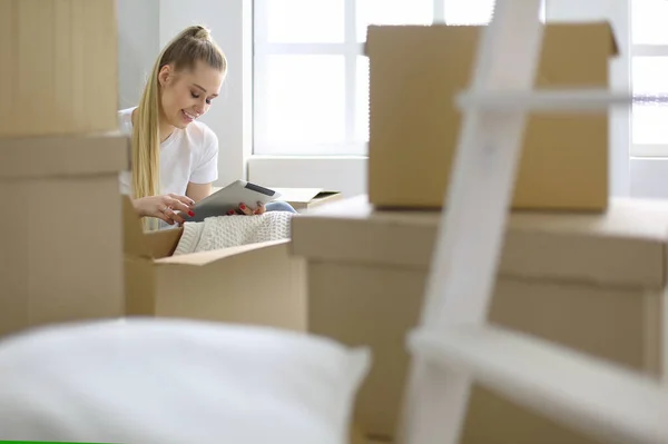 En vacker singel kvinna packa upp lådor och flytta in i ett nytt hem. En kvinna tittar på här tablett — Stockfoto