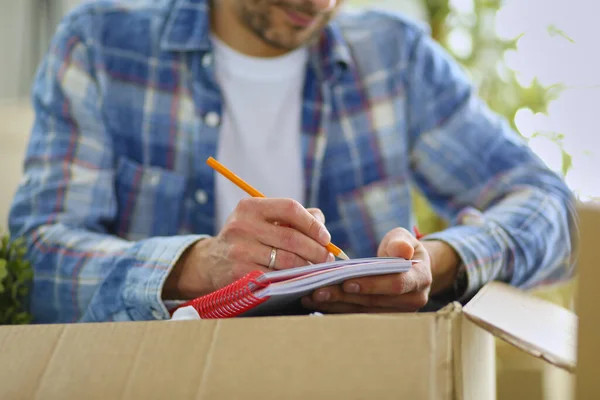 A moving man sitting on the floor in empty apartment, Among the Boxes, Checking the List of Things