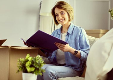 Genç bir kadın taşınıyor ve karton kutu paketliyor.