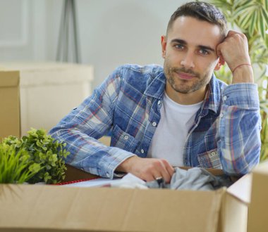 Taşınan bir adam boş bir dairede oturuyor, Kutuların arasında, eşyaların listesini kontrol ediyor.