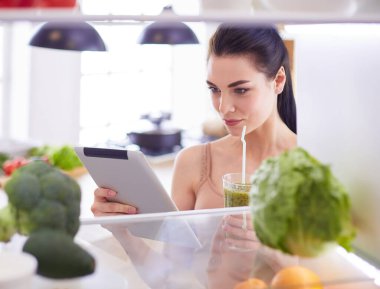 Mutfaktaki masada bir bardak lezzetli, sağlıklı smoothie ile genç bir kadın.