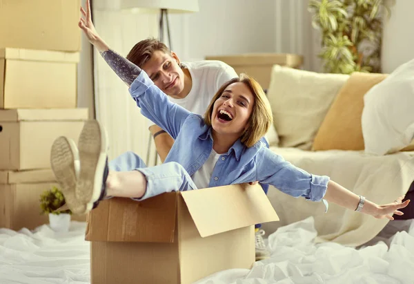 Casal feliz se divertindo e montando em caixas de papelão em nova casa — Fotografia de Stock