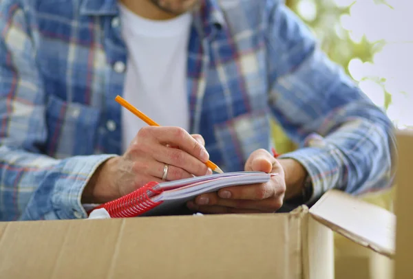 A moving man sitting on the floor in empty apartment, Among the Boxes, Checking the List of Things — Stock Photo, Image