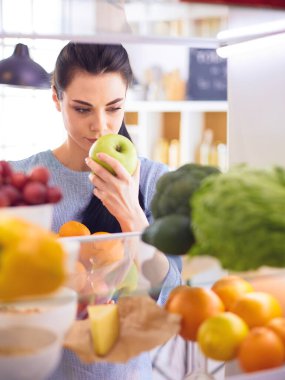 Gülümseyen kadın buzdolabından taze meyve alıyor, sağlıklı yiyecek konsepti.