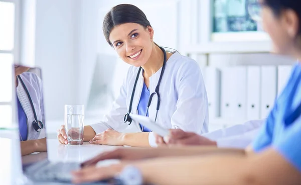 Lachende arts met behulp van een laptop werken met haar collega 's in een heldere ziekenhuiskamer — Stockfoto