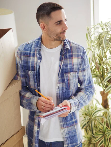 A moving man sitting on the floor in empty apartment, Among the Boxes, Checking the List of Things