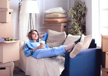 Yeni dairede kanepede uzanmış gülümseyen genç kadın.