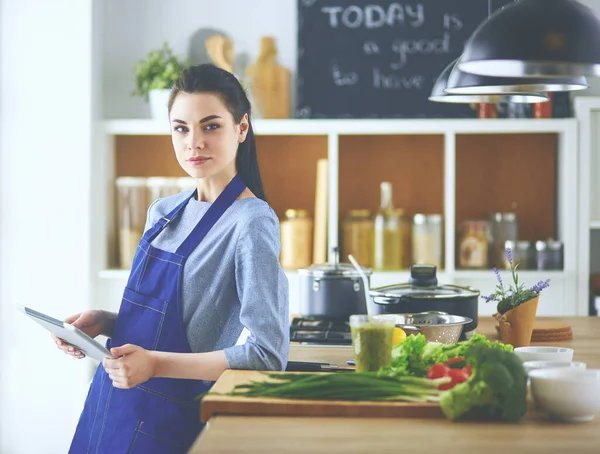 Jovem usando um computador tablet para cozinhar em sua cozinha — Fotografia de Stock