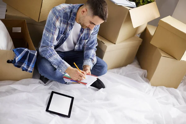 A moving man sitting on the floor in empty apartment, Among the Boxes, Checking the List of Things