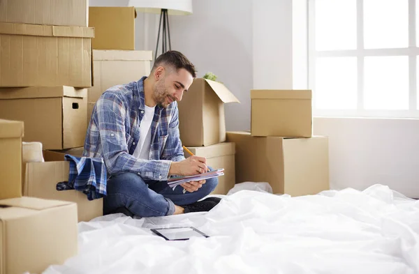 A moving man sitting on the floor in empty apartment, Among the Boxes, Checking the List of Things
