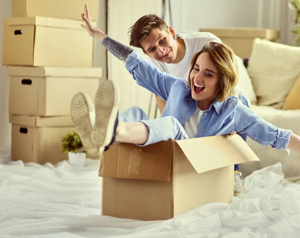 Casal feliz se divertindo e montando em caixas de papelão em nova casa — Fotografia de Stock