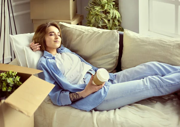 Glimlachende jonge vrouw liggend op de bank in nieuw appartement — Stockfoto