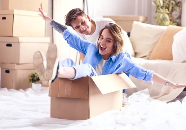 Casal feliz se divertindo e montando em caixas de papelão em nova casa — Fotografia de Stock