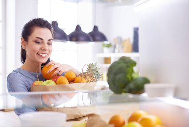 Gülümseyen kadın buzdolabından taze meyve alıyor, sağlıklı yiyecek konsepti.