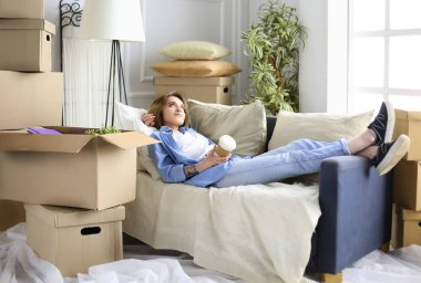 Yeni dairede kanepede uzanmış gülümseyen genç kadın.