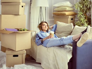 Yeni dairede kanepede uzanmış gülümseyen genç kadın.