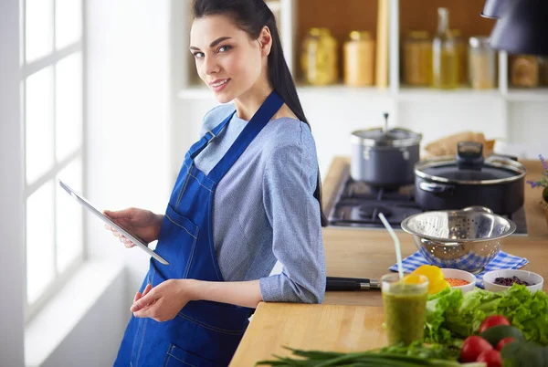 Young woman using a tablet computer to cook in her kitchen — Stock Photo, Image