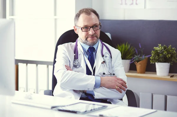 Portrét staršího lékaře sedícího za stolem — Stock fotografie