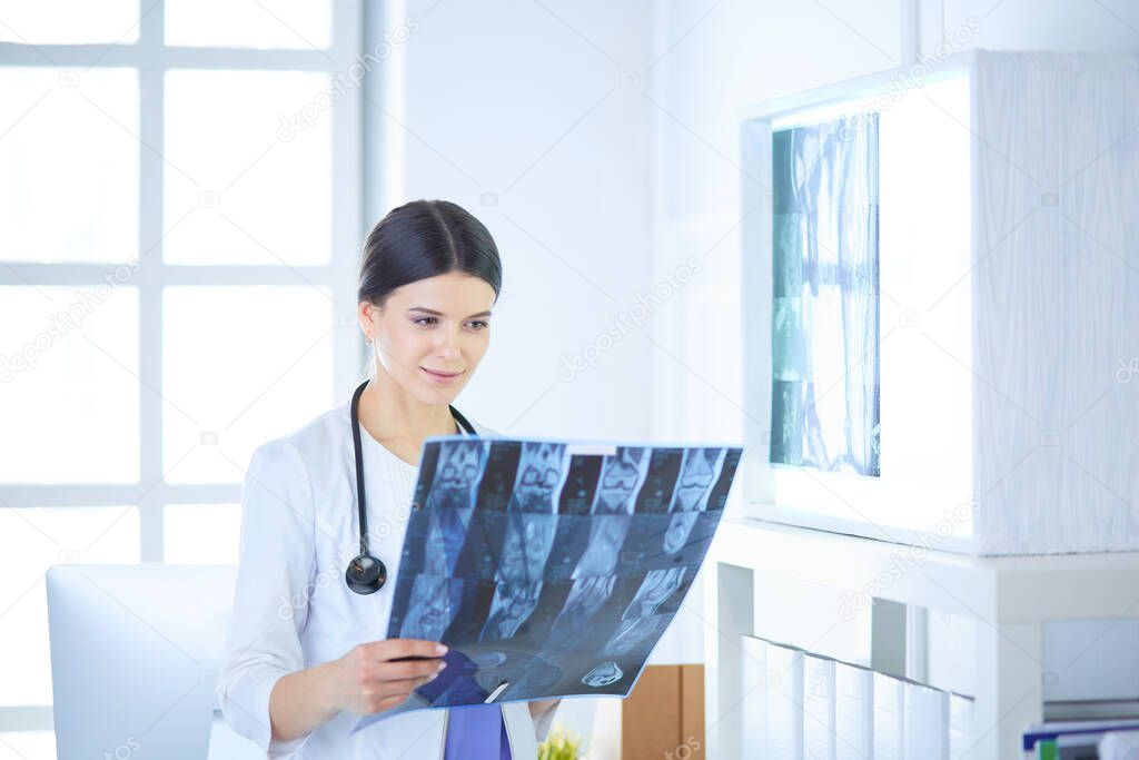Young smiling female doctor with stethoscope looking at X-ray at doctors office